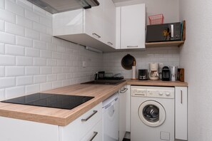 Een compacte keuken met witte kastjes, een vaatwasser, een wasmachine en een magnetron op een plank.