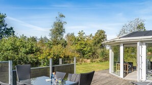 A deck with a glass-top table and wicker chairs, a covered seating area, and a view of a garden and trees. - "Martina" - 500m from the sea by Interhome (Jerup)