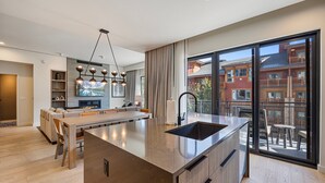 A modern kitchen with a central island, a dining area, and a large sliding glass door leading to an outdoor balcony.