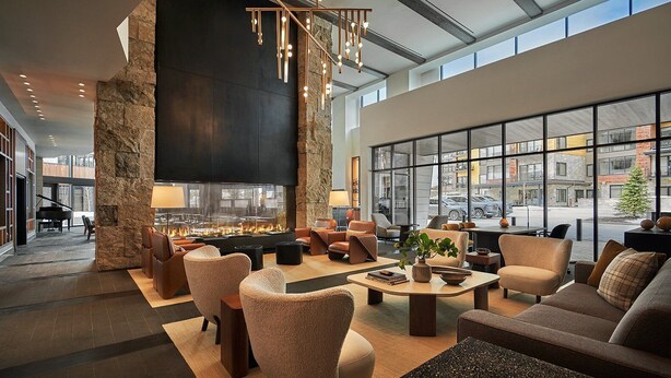 A modern lounge area with a stone pillar, comfortable seating, a fireplace, and large windows offering city views.