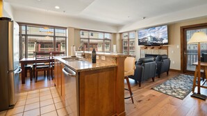 Una cocina moderna con una isla central, comedor con sillas, un sofá y un televisor en la pared.