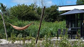 Eine Hängematte in einem Gartenbereich mit Esstisch und Stühlen, umgeben von Grünpflanzen und Bäumen.