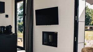 A modern living room with a flat-screen TV mounted on the wall, a fireplace, and a sliding glass door leading to an outdoor area.