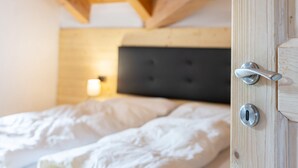 A bedroom with a wooden ceiling, a bed with white bedding, and a door with a silver handle. - Vajolet Apartment with Mountain View and Balcony (Campitello di Fassa)
