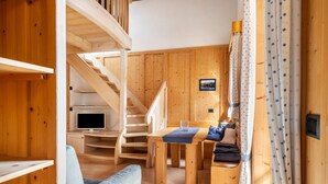 A wooden interior with a staircase, a flat-screen TV, a dining table, and a sofa. - Vajolet Apartment with Mountain View and Balcony (Campitello di Fassa)