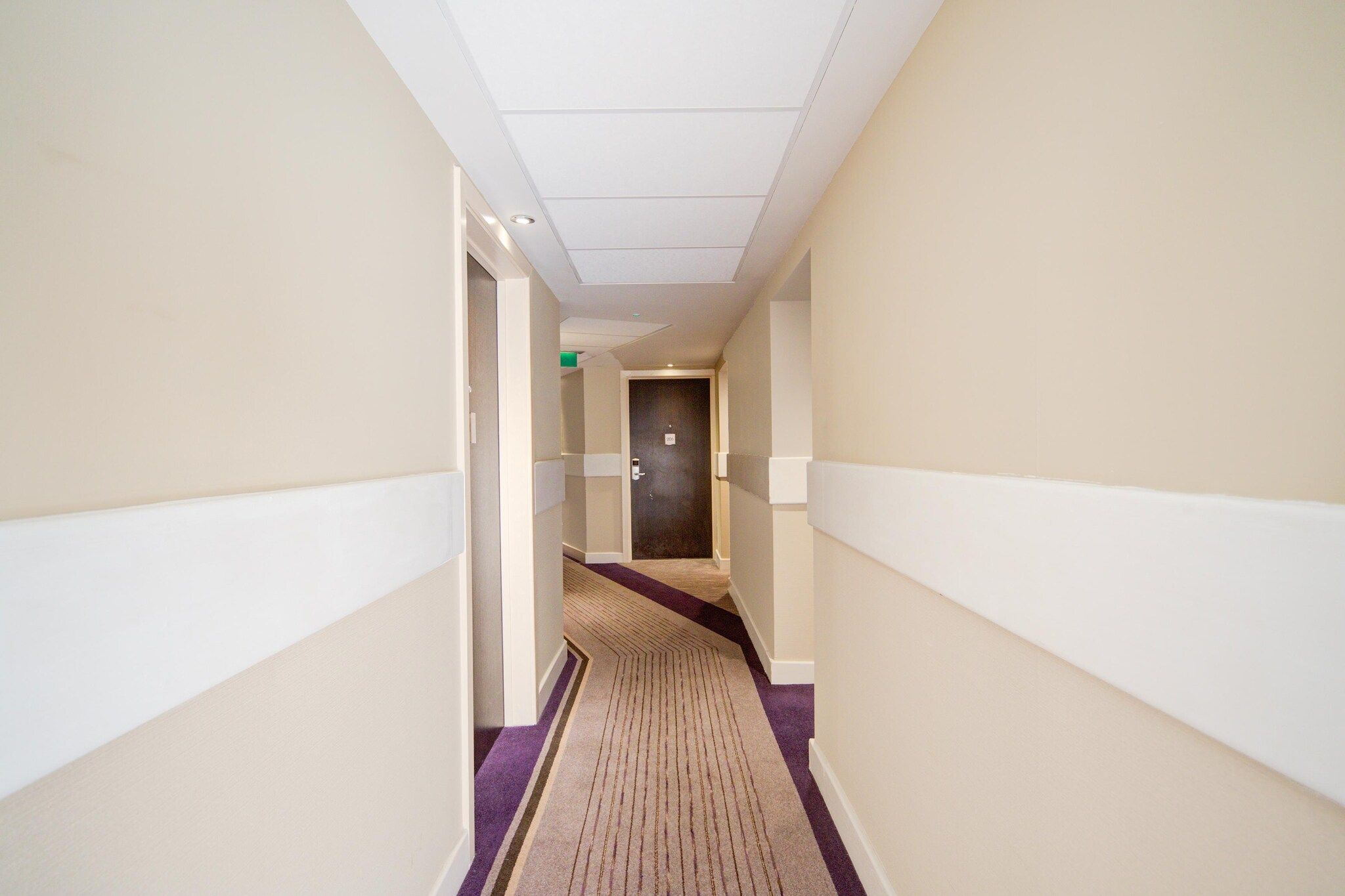 A hotel hallway with a carpeted floor, doors on both sides, and a ceiling with recessed lighting.