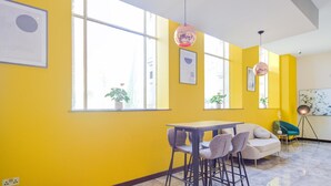 A bright yellow room with large windows, a table with chairs, and a sofa.