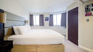 A hotel room with a large bed, a bedside table, a wardrobe, and a door leading to another room.