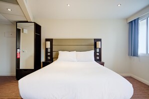 A hotel room with a large bed, a nightstand, a mirror, and a window with curtains. - Belvilla Newport City Centre Hotel - Deluxe Double Room (Newport)