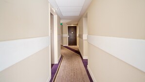 A hotel hallway with a carpeted floor, white walls, and a door at the end.