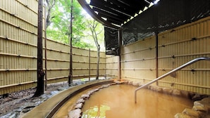 Perinteinen japanilainen onsen-kylpylä, jossa on kivinen kylpyallas, jonka ympärillä on bambuseinät ja yläpuolella puukatto.