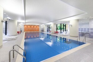 A large indoor swimming pool with clear blue water, surrounded by tiled walls and a ceiling with recessed lighting. - Raconter Arima (Kobe)