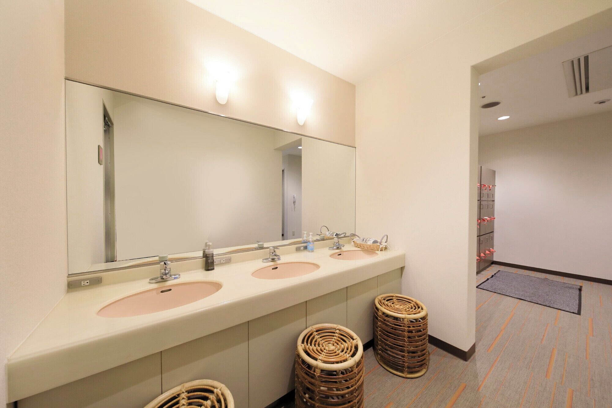 Un baño de hotel con tres lavamanos, un espejo grande y cestas de mimbre.