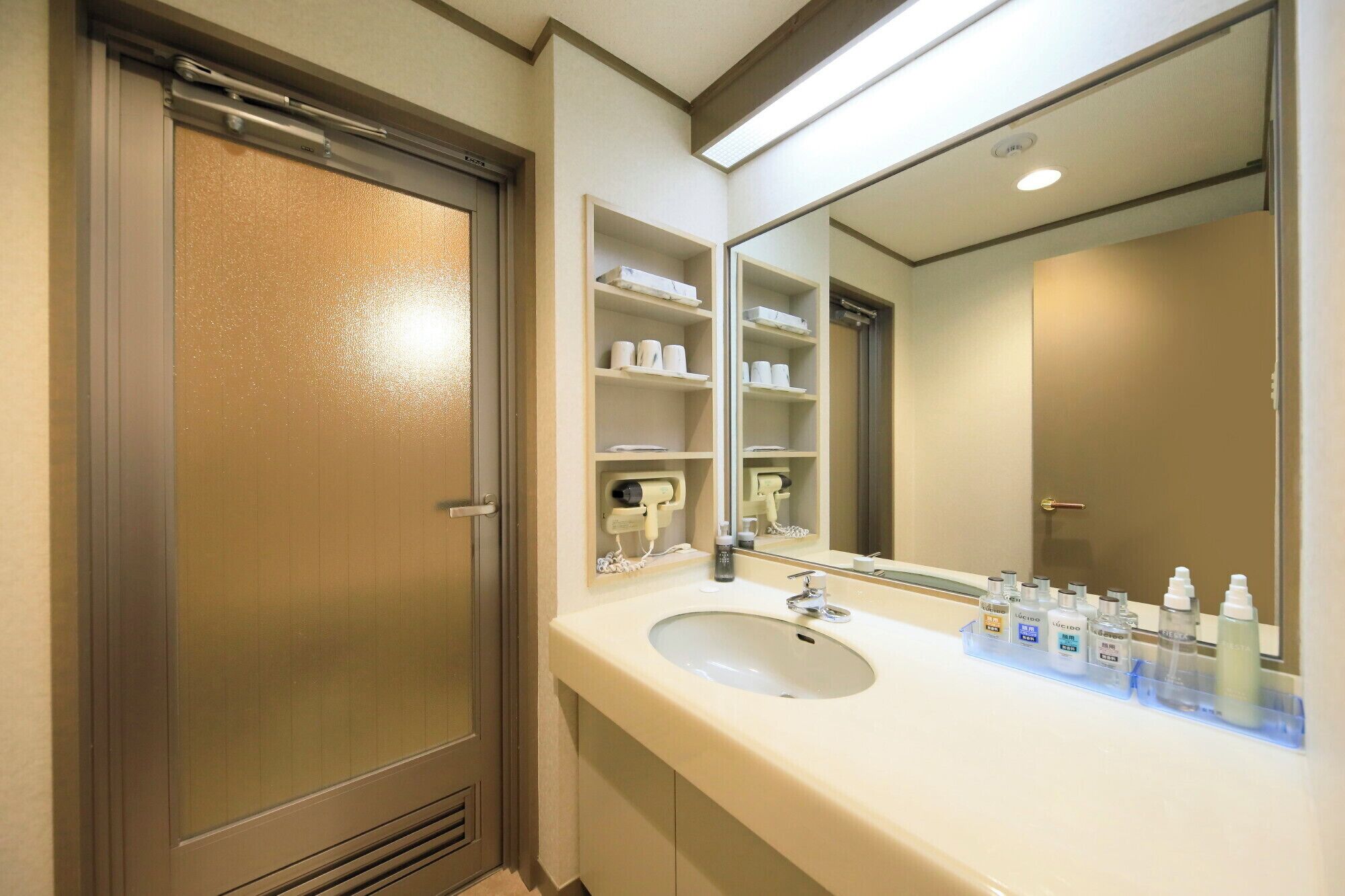 A hotel bathroom with a large mirror, a sink, and shelves with toiletries.