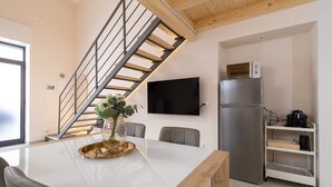 Una cocina moderna con un refrigerador empotrado, una mesa de comedor con sillas, un televisor montado en la pared y una escalera con barandilla.