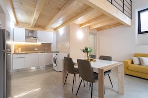 Une cuisine moderne équipée d’un lave-linge intégré, un coin repas avec une table et des chaises, et un canapé jaune.