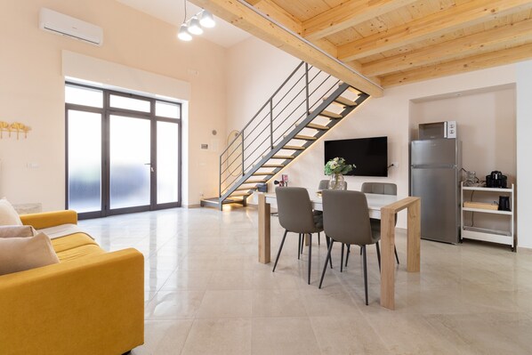 A modern living space with a staircase, a dining area, a sofa, and a kitchen.