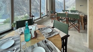 A dining area with large windows, wooden beams, and a mountain view. - Tara Mountain Sarai (Kargil)