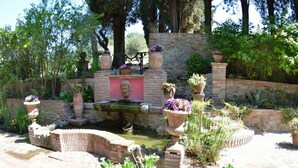 Un jardín con una fuente de piedra, plantas en macetas y un camino de ladrillo.