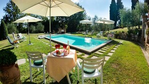 Zona junto a la piscina con sillones de descanso, sombrillas y una mesa lista para comer.