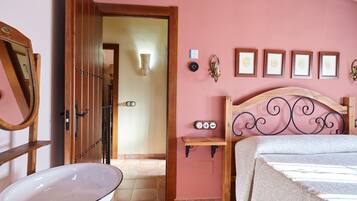A bedroom with a bed, a bedside table, a mirror, and a wall-mounted clock.