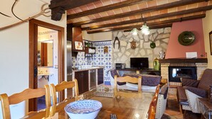 A living room with a fireplace, a dining area with a table and chairs, and a kitchen area with a tiled backsplash. - Rural House 'La Acacia' with Private Pool, Wi-Fi and Air Conditioning (Martos)