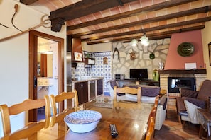 Een woonkamer met een open haard, een eetgedeelte met een tafel en stoelen, en een keuken met een betegelde achterwand.