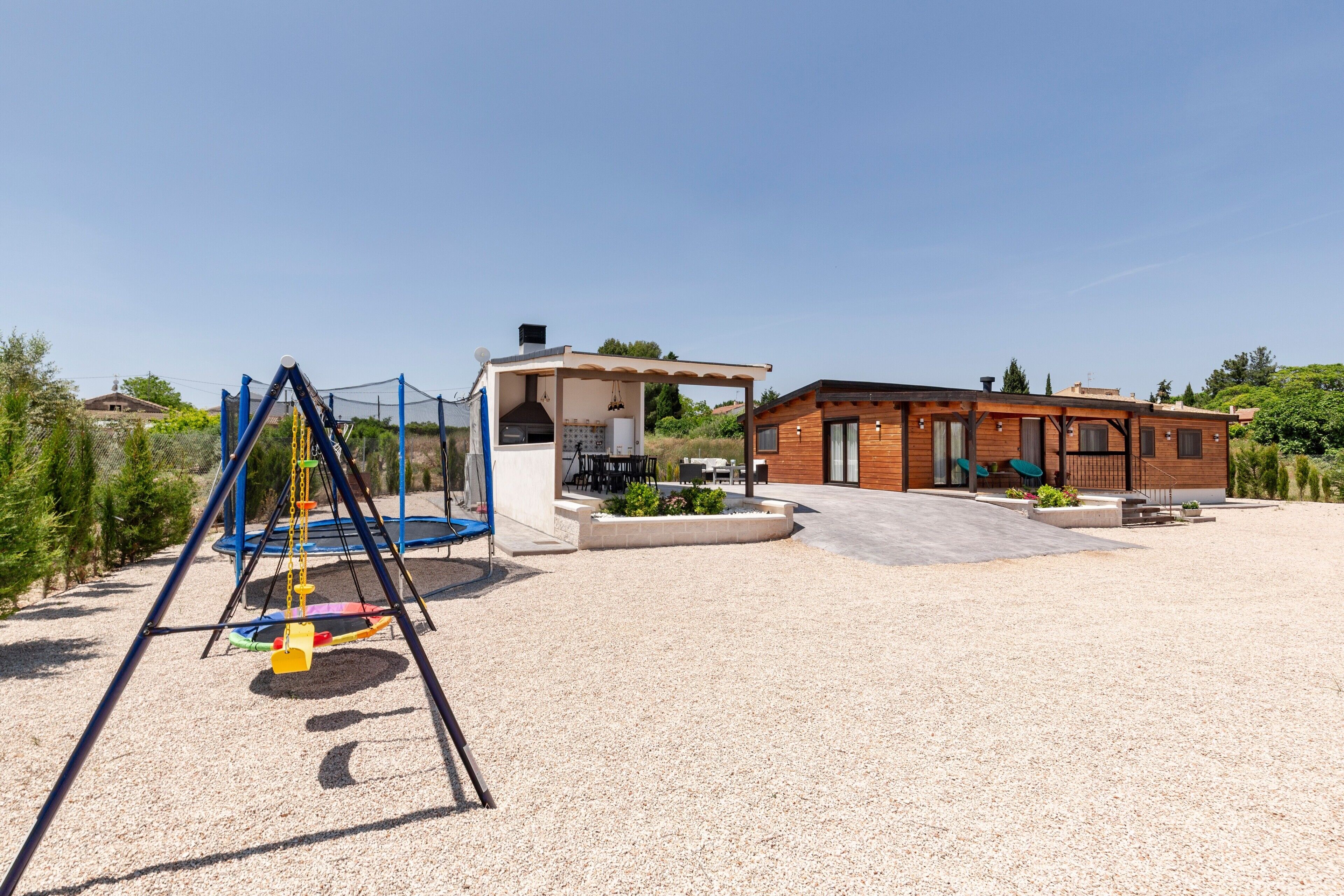 A playground with swings and a climbing structure, a covered seating area, and a building with a patio.