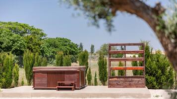 Un jacuzzi de madera y un banco de madera en un jardín con cerca y árboles.