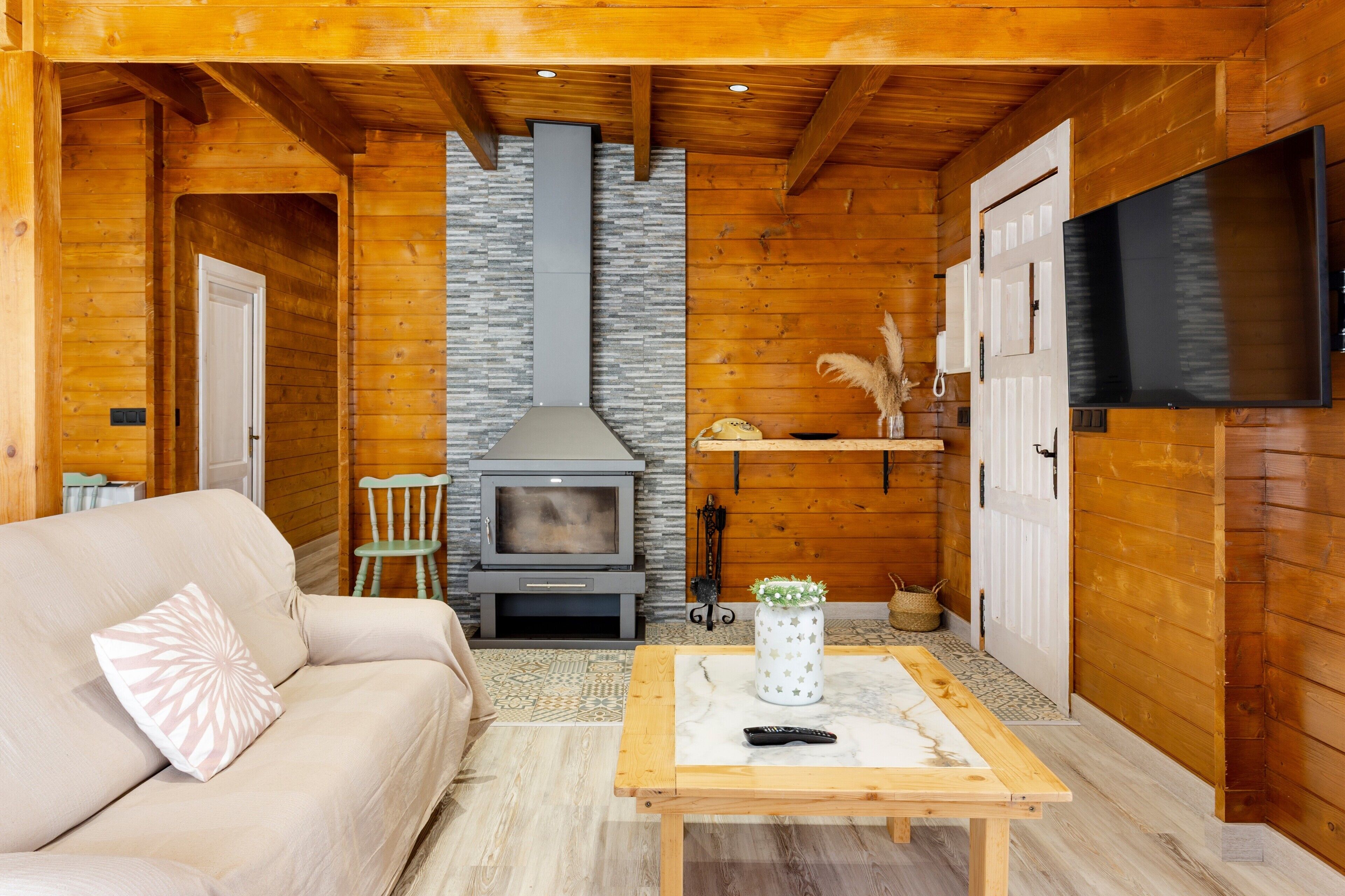 L’intérieur d’un chalet en bois, avec un canapé, une table, une cheminée et un téléviseur fixé au mur.