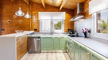 A modern kitchen with wooden beams, green cabinets, a stainless steel dishwasher, and pendant lights.