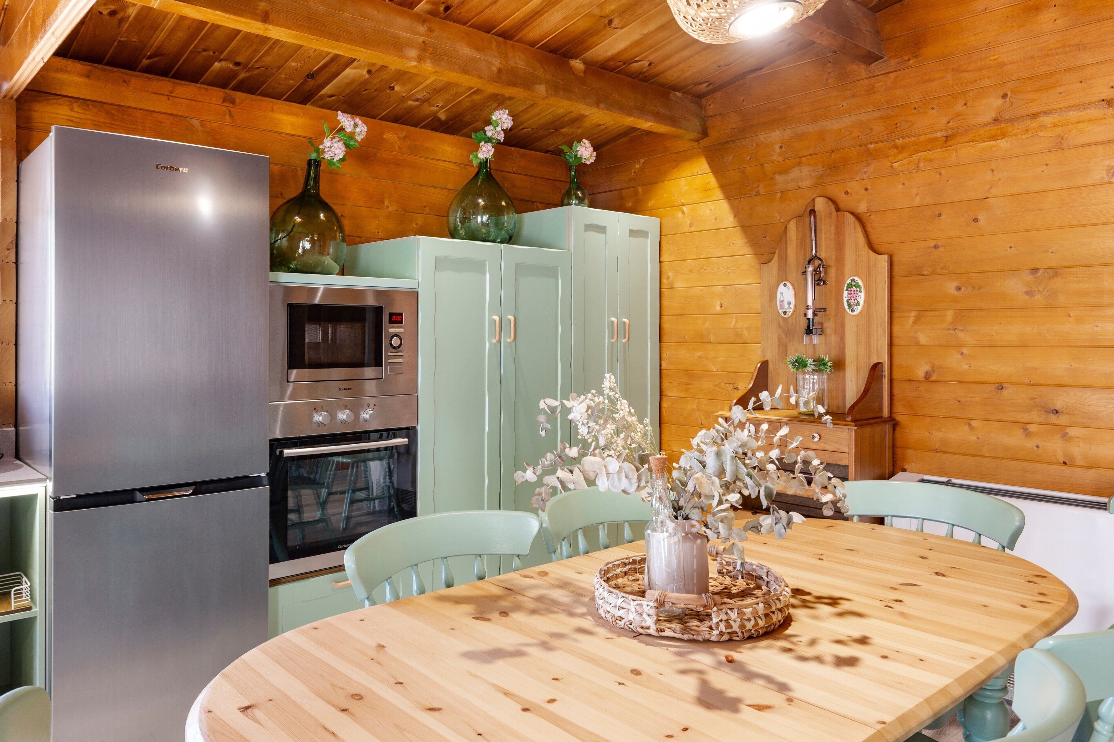 Una cocina con un refrigerador, horno y microondas de acero inoxidable. Hay una mesa de comedor con sillas y un florero con flores.