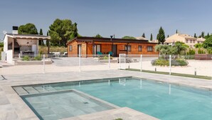 Una piscina con muelle de madera, un edificio pequeño con zona de cocina y un jardín vallado.