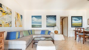 A living room with a sofa, a glass coffee table, a dining table with chairs, and artwork on the walls. - Holiday Home 'Iris 8 Is Molas Golf Resort' with Sea View, Private Terrace and Wi-Fi (Is Molas)