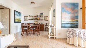 A dining area with a wooden table and chairs, a small cabinet, and a painting on the wall. - Holiday Home 'Iris 8 Is Molas Golf Resort' with Sea View, Private Terrace and Wi-Fi (Is Molas)