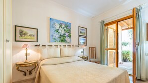 A bedroom with a bed, a nightstand, a lamp, and a painting on the wall. - Holiday Home 'Iris 8 Is Molas Golf Resort' with Sea View, Private Terrace and Wi-Fi (Is Molas)
