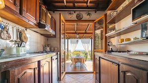 A kitchen with wooden cabinets, a tiled floor, and a view to an outdoor patio. - Holiday Home 'Iris 8 Is Molas Golf Resort' with Sea View, Private Terrace and Wi-Fi (Is Molas)