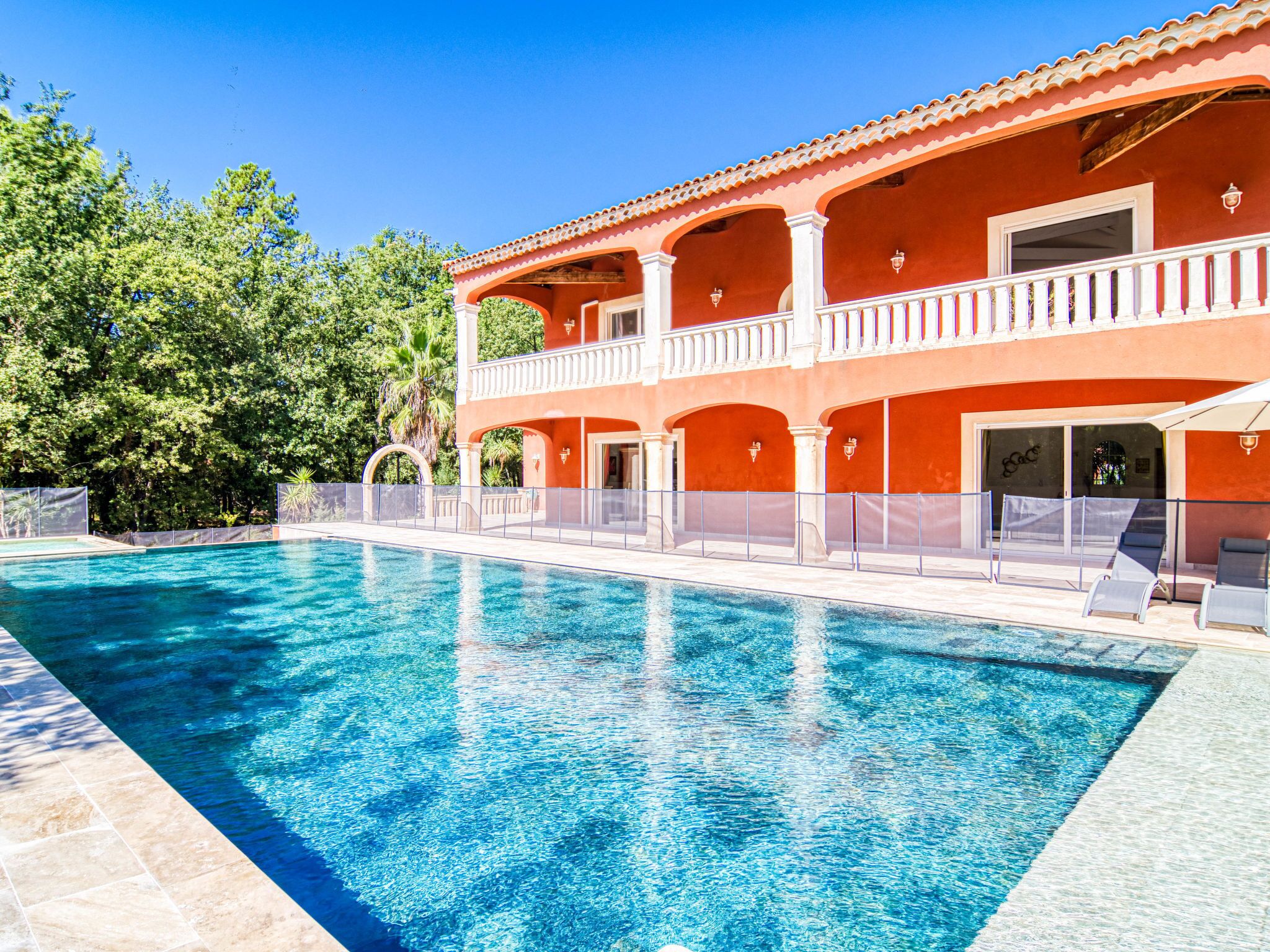 A swimming pool with a clear blue water surface, surrounded by a white fence.