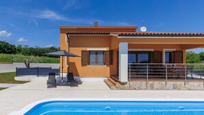 Et moderne hus med swimmingpool, udendørs møbler og en overdækket terrasse.