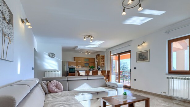 En rummelig opholdsstue med sofa, sofabord og udsigt til køkken og balkon.