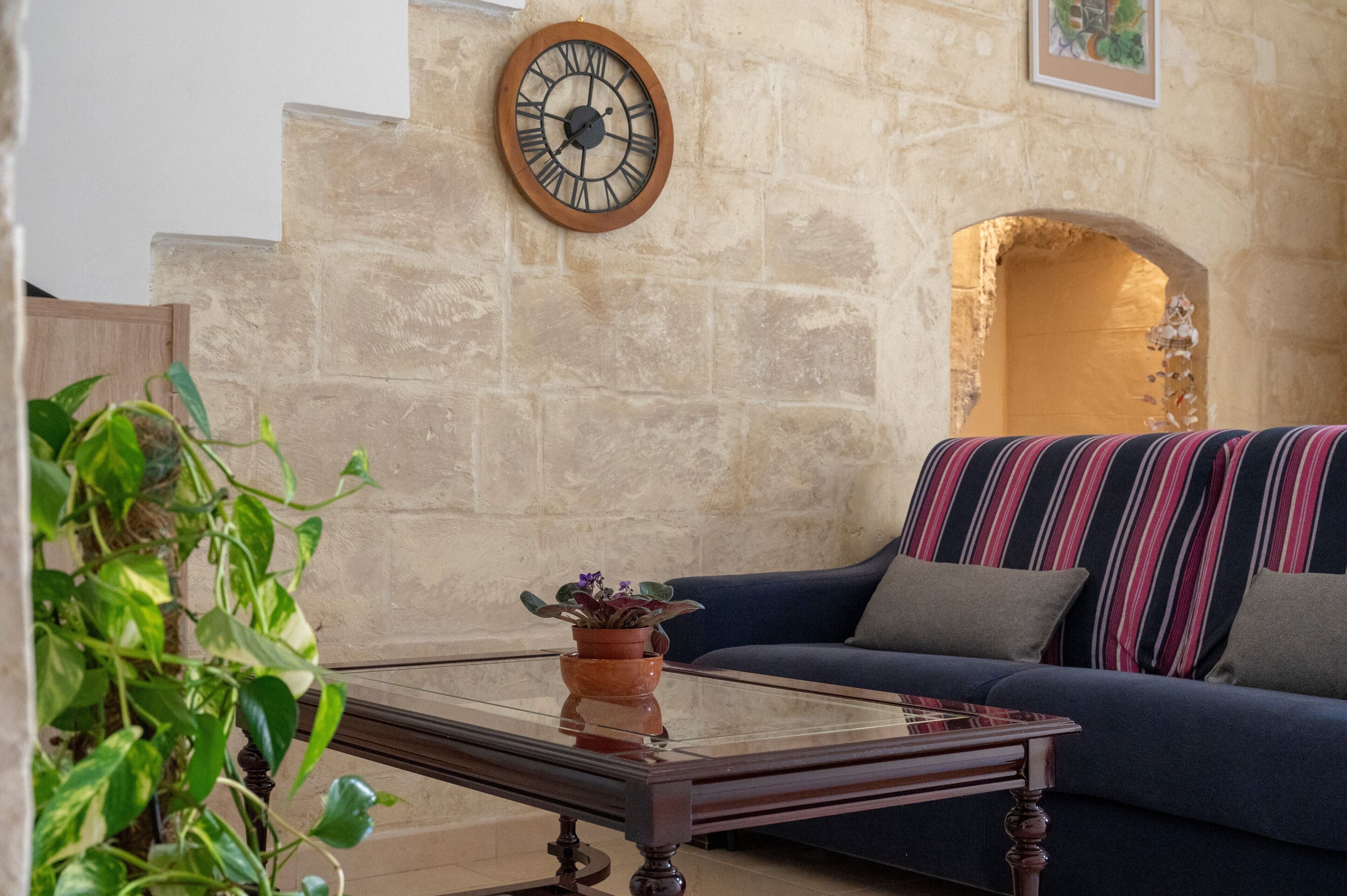 A living room with a stone wall, a blue sofa, a wooden clock, and a glass coffee table with a potted plant.
