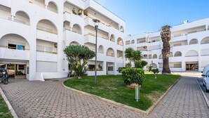 Un edificio de varios pisos con un patio, una palmera y un coche estacionado.