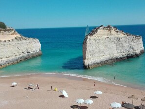A beach with white cliffs, clear turquoise water, and a sandy shore with umbrellas and people. - Apartment 'Dreaming Of Algarve' with Shared Pool, Shared Garden and Wi-Fi (Porches)