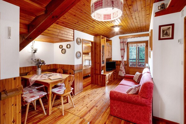A wooden interior with a dining table, chairs, a sofa, and a television.