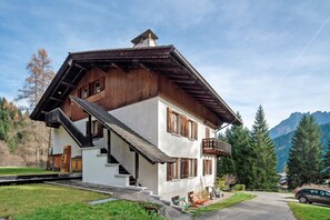 Une maison en bois à deux étages, dotée d’un balcon, d’un escalier et surplombant un paysage montagneux.