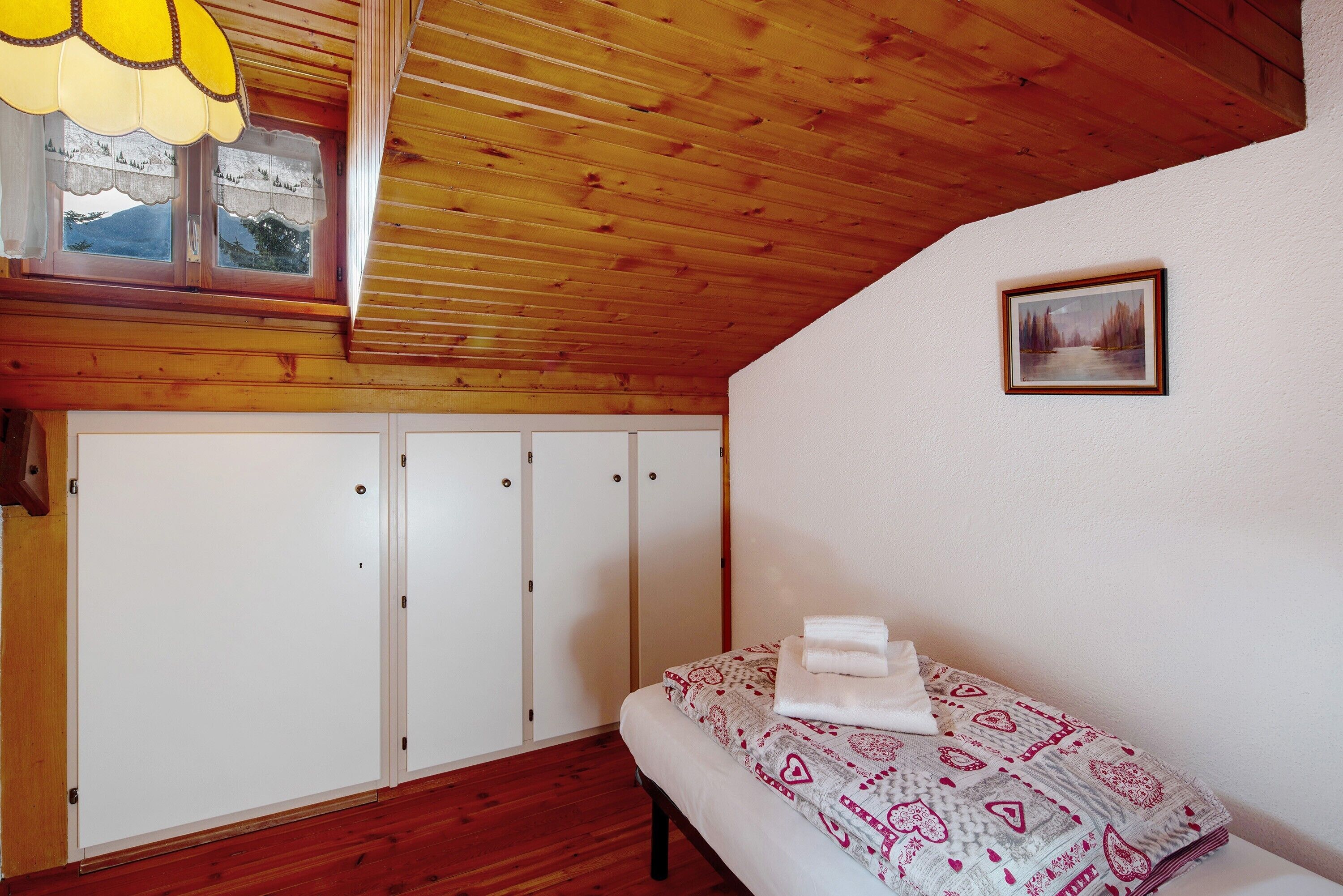 Una camera da letto con soffitto in legno, un letto con biancheria a motivi, una finestra con vista e un quadro appeso al muro.