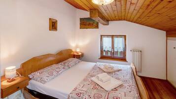 A bedroom with a wooden ceiling, a bed with patterned bedding, a nightstand, a wall-mounted picture, and a window with a view.