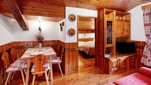 A wooden interior with a dining table, chairs, a bed, a TV, and a red sofa. - Apartment 'Appartamento Palmina' with Mountain View, Shared Garden and Wi-Fi (Falcade)