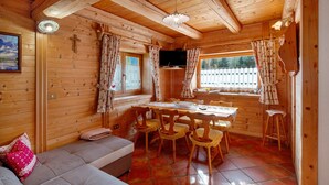 A wooden cabin interior with a sofa, dining table, chairs, and a TV.