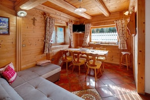 Ein Holzblockhaus-Innenraum mit einer Couch, einem Esstisch, Stühlen und einem Fernseher.